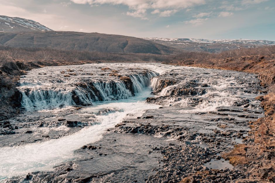 Breathtaking view of a waterfall cascading through rugged Icelandic terrain under a clear sky.