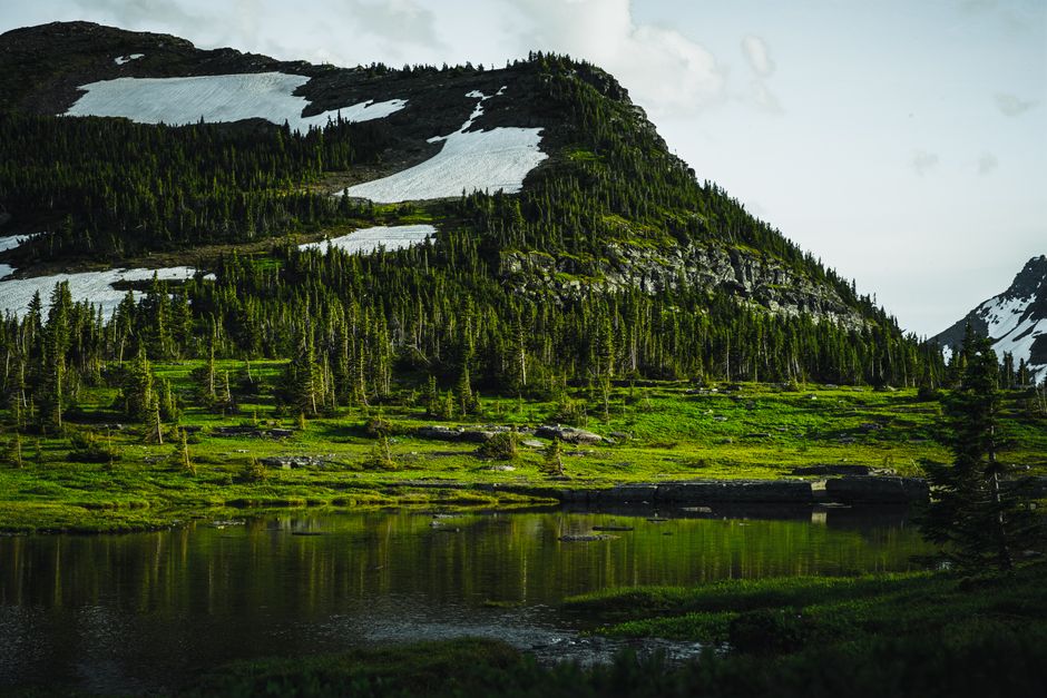 A breathtaking view of a mountain with snow patches and a reflective lake beneath, capturing nature's serene beauty.