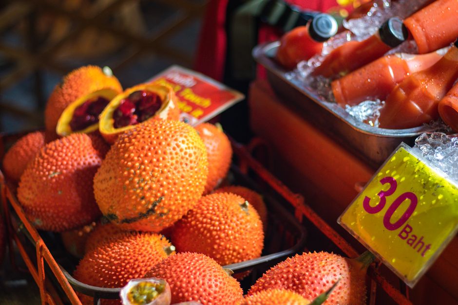 Vivid display of exotic gac fruits and fresh juice bottles at a night market stall.