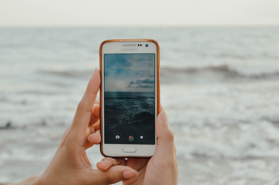 Hands holding a smartphone taking a picture of the ocean. Perfect for technology and travel themes.