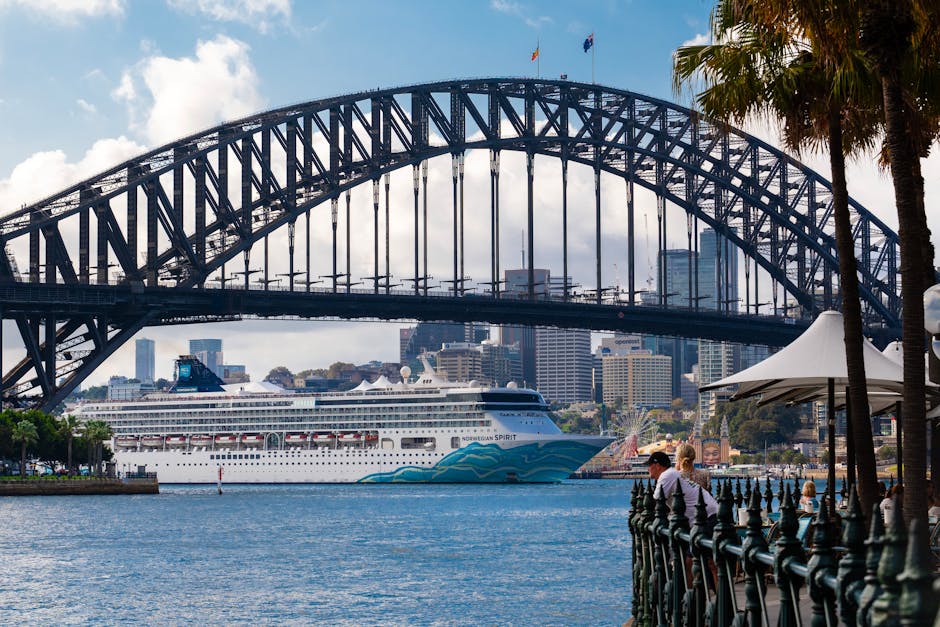 A bustling view of a cruise ship passing under the iconic Sydney Harbour Bridge in Australia.