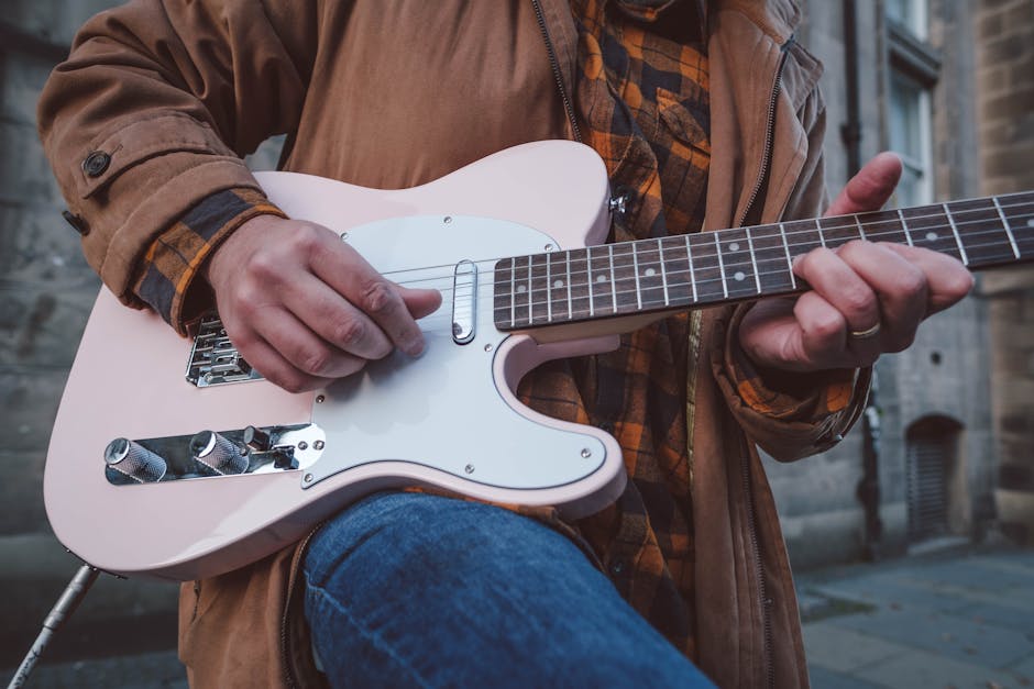 A man in a jacket plays an electric guitar outdoors, showcasing a casual music vibe.