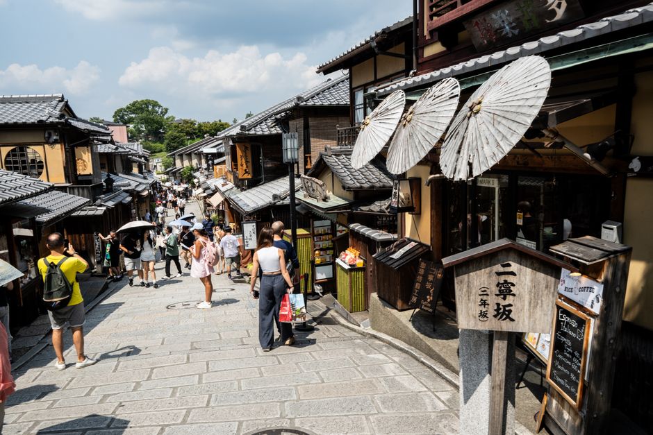 Bustling street in Kyoto with traditional shops and parasols under a bright sky.