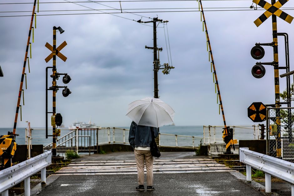Person with umbrella at a railway crossing by the sea in Matsuyama, Japan.