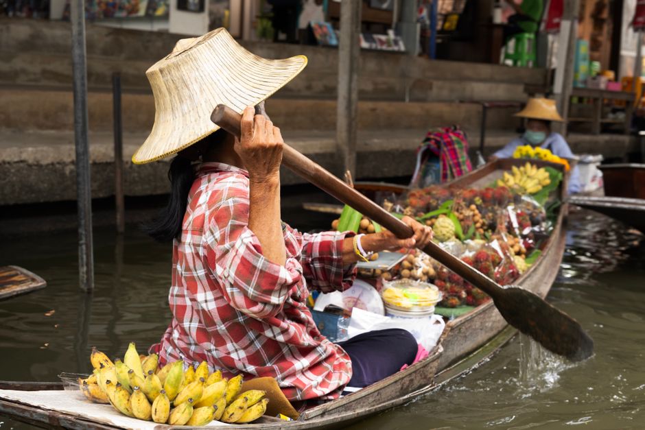 Woman paddling boat at a vibrant floating market in Bangkok, Thailand.