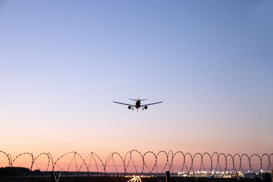 A serene shot of an airplane landing over a barbed wire fence at sunset in Mārupe, Latvia.