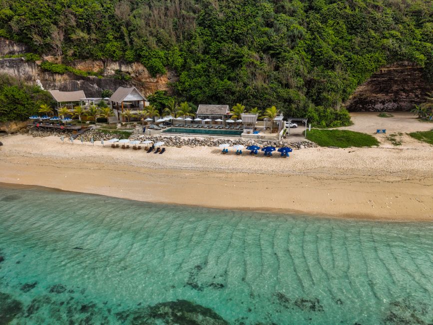 Aerial photo of a picturesque beachfront resort in Bali, showcasing clear waters and lush greenery.