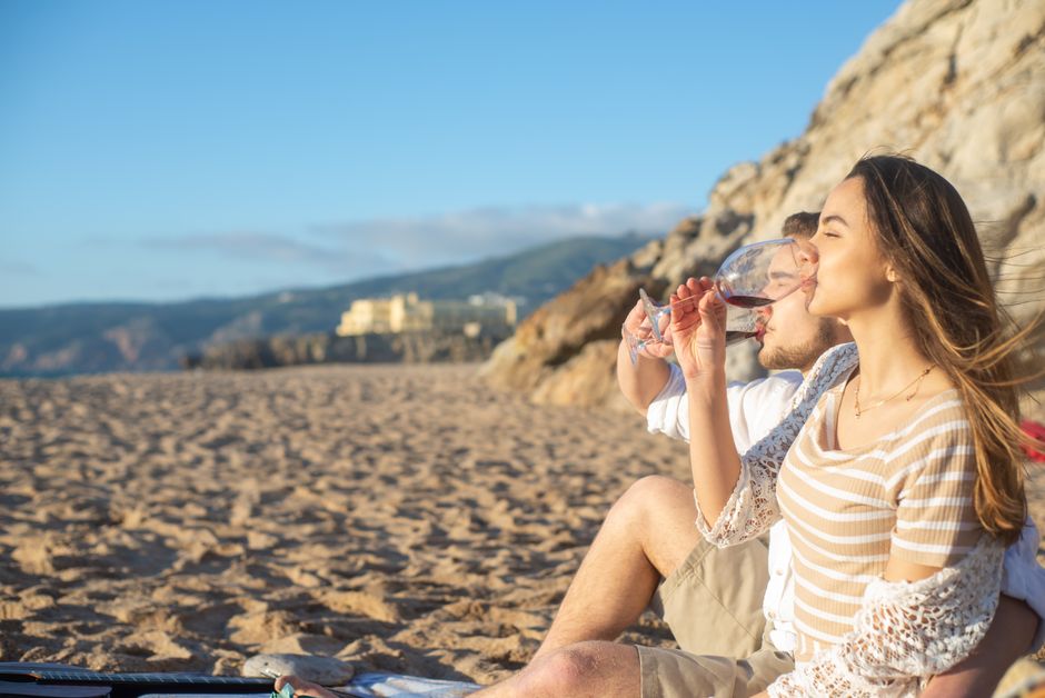 Couple enjoying a romantic wine picnic on a Portuguese beach during a sunny day.