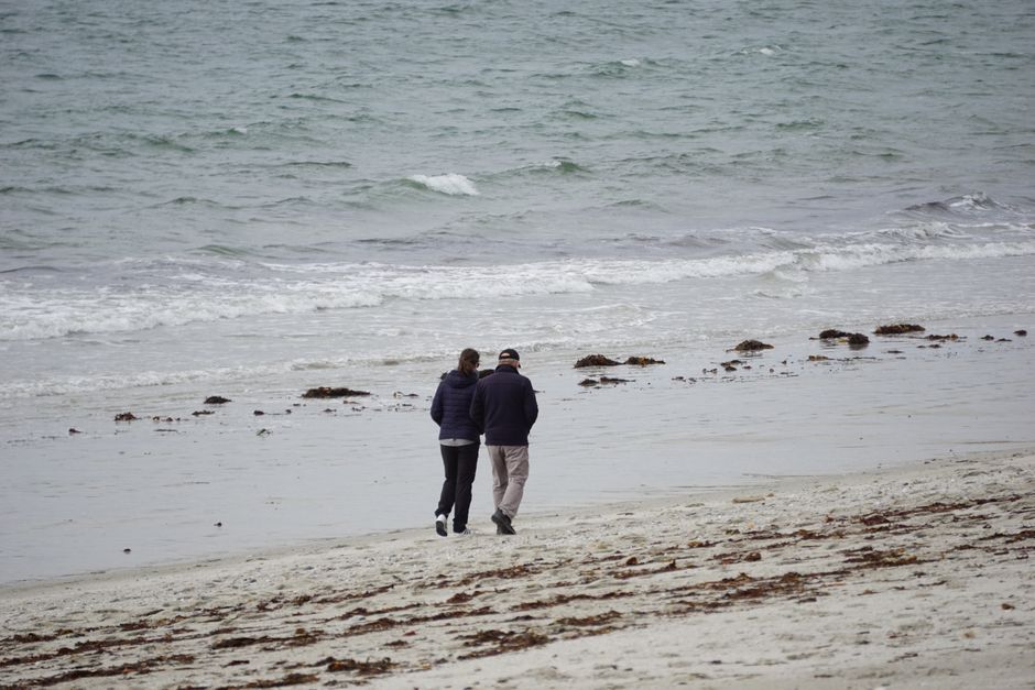 A couple strolling along a serene sandy beach near the ocean during the day.