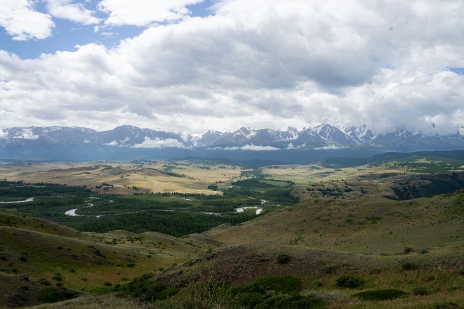 Breathtaking landscape photo of a vast valley and snow-capped mountains under a cloudy sky.